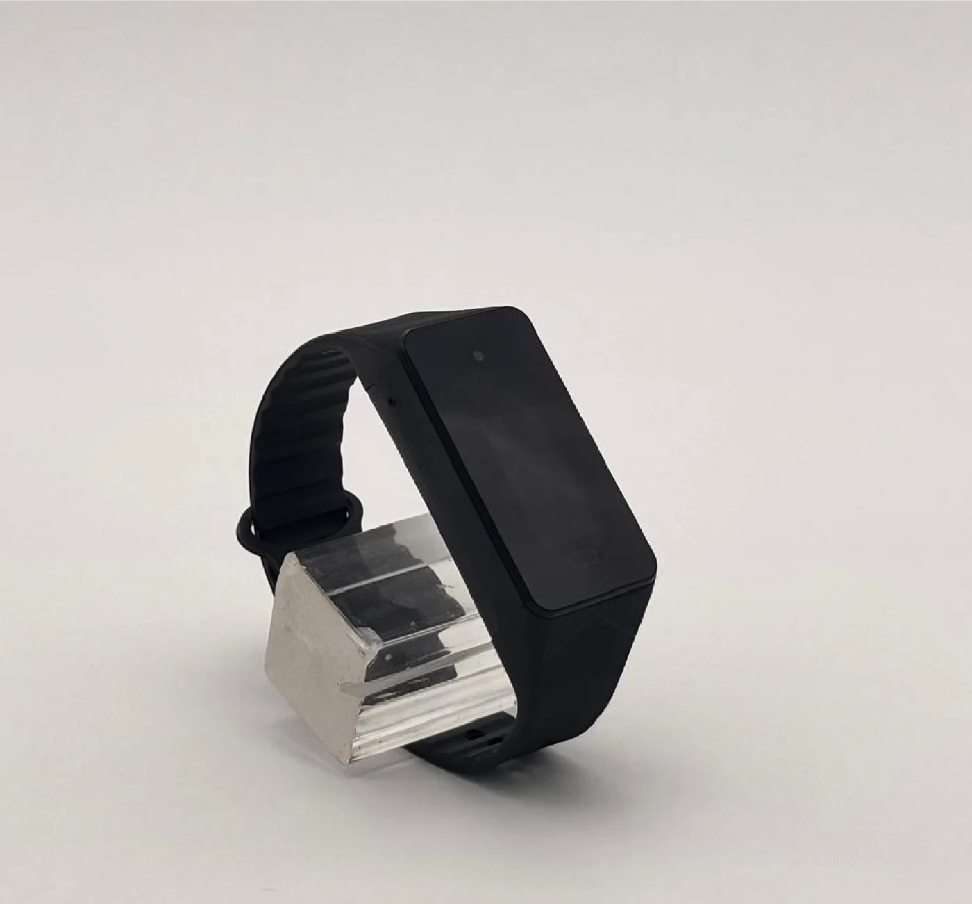 Black rectangular device with an adjustable strap, displayed on a clear stand.