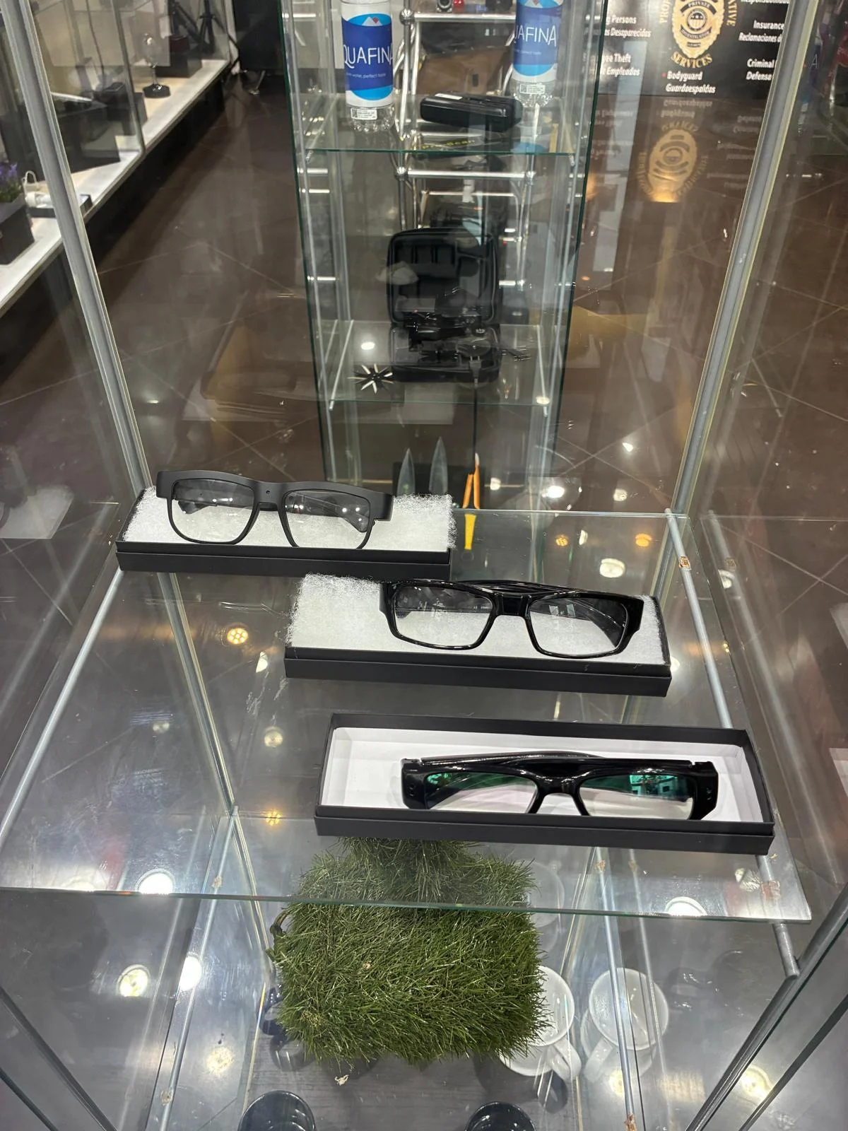 Three pairs of black-framed glasses displayed in separate boxes inside a glass case.
