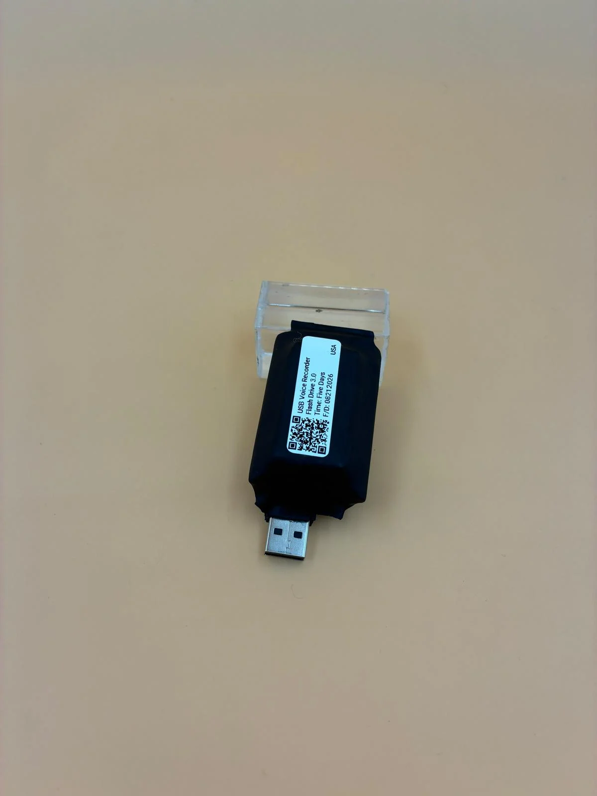 A compact recorder on a clear support, with its label and USB connector visible.